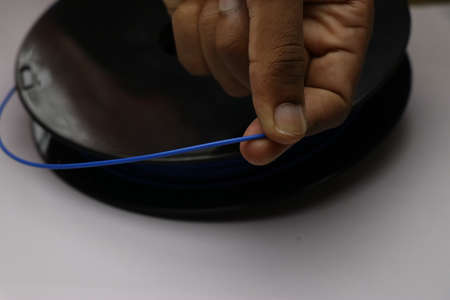 Blue color filament material held in hand from a spool. 3D Printer use these material to create...