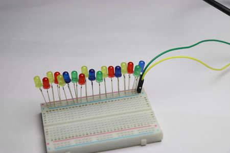 Multicolor LED are connect to solderless breadboard laid flat on white background which shows...