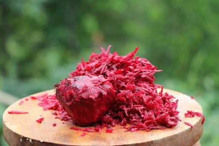 Heap of grated red beetroot in wooden cutting board on nature background