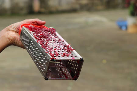 stainless steel grater with pieces of red beetroot held in hand. Grater for vegetable shreddingの写真素材