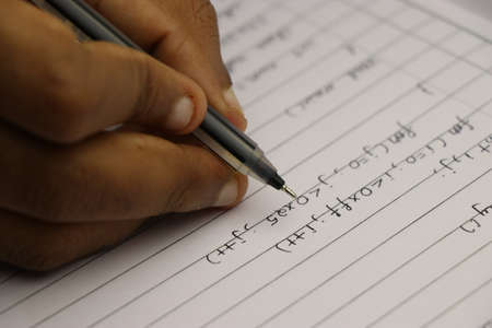 Hand of student writing computer programs on paper with black pen
