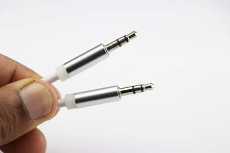 Close up of silver 3.5 mm audio jack cable held in hand on white background. Metal silver aux audio...