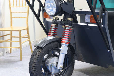 Front part of an electric tricycle with suspension springs and headlights view. Electric auto...