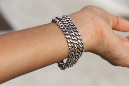 Pure silver chain that is worn as a bracelet on hand exposed to natural light. Silver chain with details of chain linksの写真素材