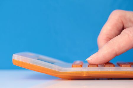 Fingers on an orange calculator closeup on a blue backgroundの写真素材