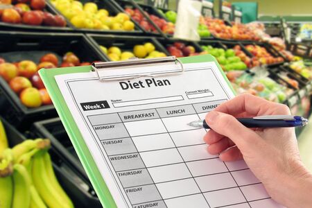 Hand with Pen Writing a Diet Plan by Supermarket Fruitの写真素材