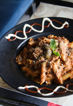 Penne pasta with sauce and fresh parmesan on black plate.の写真素材