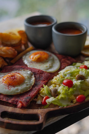 Breakfast with fried egg, bacon and vegetables on a wooden board.の写真素材