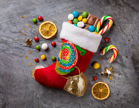 Christmas sock with candies, lollipops and marshmallows on stone backgroundの素材
