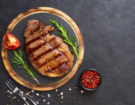 Grilled beef steak with rosemary and spices on black stone background. Top view with copy spaceの素材