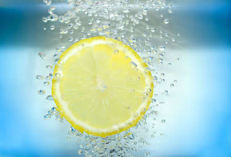Lemon slice in water with air bubbles on blue background.の写真素材