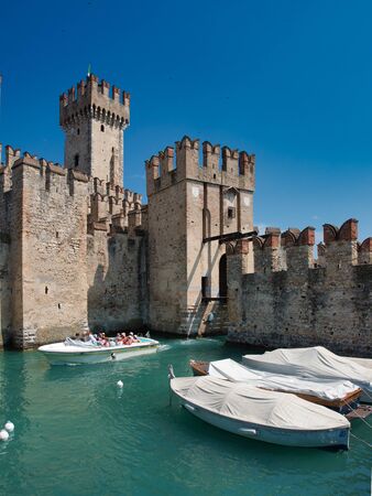 Boat with turisitas on board passes through the front of the Scaligero Castle on a summer morningのeditorial素材