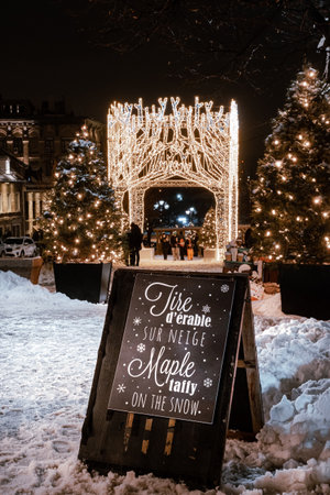 Montreal, Quebec, Canada - January 3, 2021 A sign offering Maple taffy on the snow in the place Jacques-Cartier in Old Montreal with Christmas lights and winter decorations in the backgroundのeditorial素材