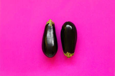 Pair of aubergines isolated in fuchsia background viewed from above - flatlay look