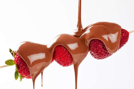 Strawberry skewer with melted milk chocolate being poured isolated in studio with a white backgroundの写真素材