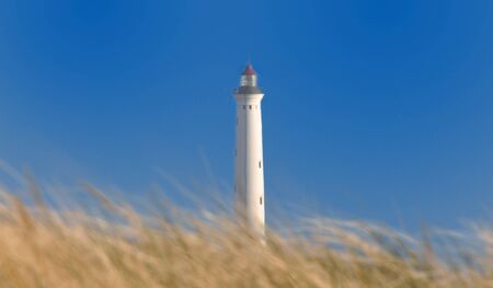A white lighthouse behind a dune.の写真素材