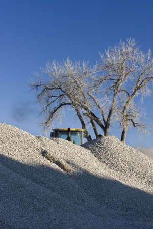 pile of gravel at a road construction with a tree and a bulldozer working  behind it, blue sky, copy spaceの写真素材