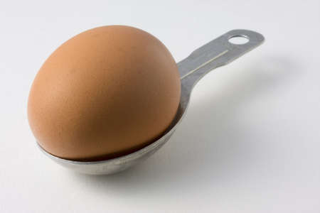 brown egg on a measuring aluminum tablespoon, white paper background with some texture and shadowの写真素材