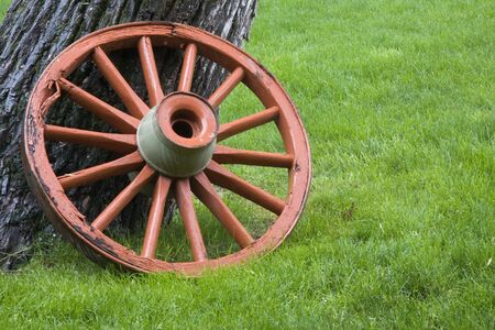 old, wheathered wagon wheel painted orange against green grass in rainの写真素材