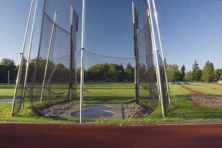 green grass athletic field with a hammer throw cage and long jump sand pit, early morning lightの写真素材