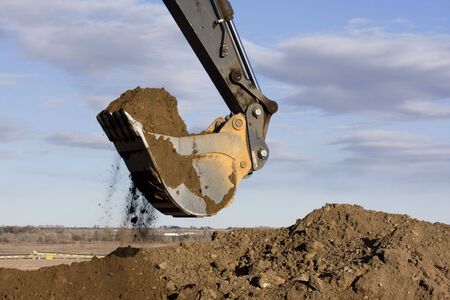 Excavator arm and scoop full of dirt at construction site against blue, partially cloudy, skyの写真素材