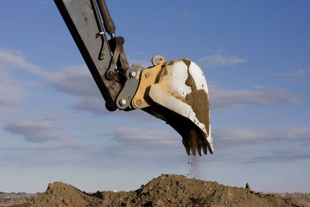 Excavator arm and scoop digging dirt at construction site against blue, partially cloudy, skyの写真素材