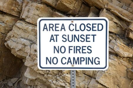 area closed at sunset, no fires or camping - whte warning sign in front of climbing rock cliffの写真素材