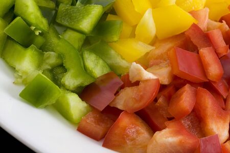 diced green, red and yellow bell pepper on a white plate ready for cooking or saladの写真素材