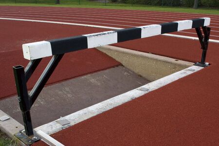 red running tracks with white and black steeplechase barrier and water jump pitの写真素材
