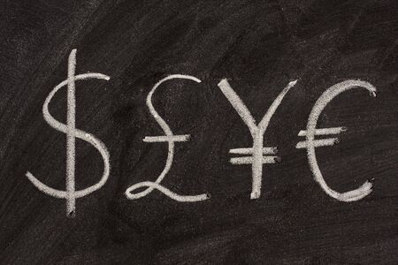 dollar, pound, yen and euro symbols sketched with white chalk on a black boardの写真素材