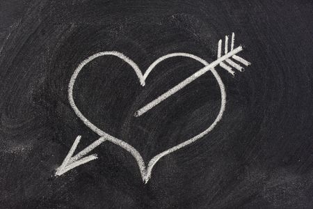 heart pierced by arrow, a modern symbol of sexual love, sketched with white chalk on blackboard
