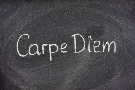 Enjoy life before it's too late, existential cautionary Latin phrase, Carpe DIem, a quote from Horace, handwritten with white chalk on blackboard.の写真素材