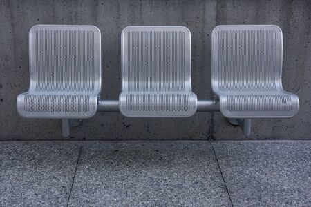 three modern perforated metal chairs against a concrete wall の写真素材