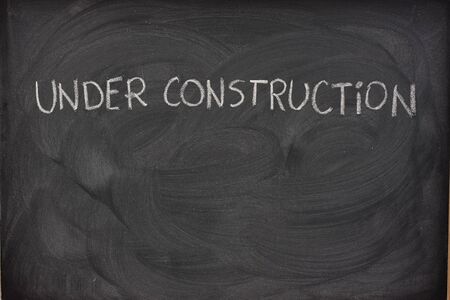 under construction phrase handwritten with white chalk  on a blackboard with eraser smudges and copy space belowの写真素材
