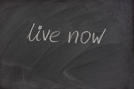 live now phrase handwritten with white chalk on blackboard with strong patterns of eraser smudgesの写真素材