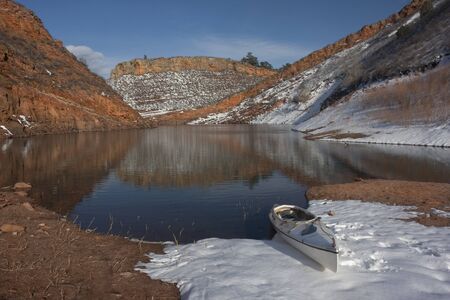 canoe and Colorado mountain lake (Horestooth Reservoir near Fort Collins)  in early spring with red sandstone cliffs and snowの写真素材