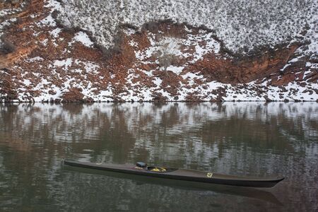 long, narrow, carbon fiber, racing sea kayak on mountain lake with high red sandstone cliffs covered by snow, Horsetooth Reservoir near Fort Collins, Colorado, thirteen - temporary race number placed on deck by myselfの写真素材