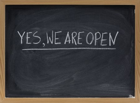 "yes, we are open" - business invitation handwritten with white chalk on blackboard with eraser smudgesの写真素材