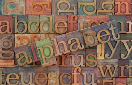 the word of alphabet across a background of vintage wooden letterpress type blocks, stained by color...
