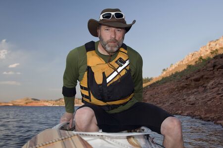 mature male boarding his canoe on a mountain lake with red sandstone cliffs (Horsetooth Reservoir near Fort Collins, Colorado)の写真素材
