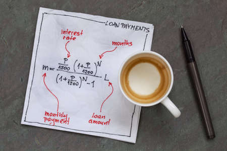 loan payment equation sketched on a white cocktail napkin with empty coffee cup on a slate stone tableの写真素材