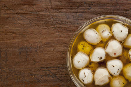 balls of mozzarella cheese marinated in oil with seasoning, glass bowl on weathered wood backgroundの写真素材