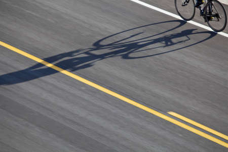 abstract bicyclist shadow on an asphalt highway with yellow lineの写真素材