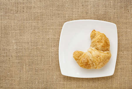 croissant roll on a white china plate against burlap canvas boardの写真素材
