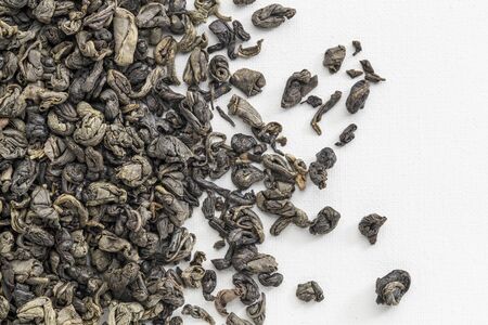 background texture of loose leaf Chinese gunpowder (pearl) green tea spilled over white artist...