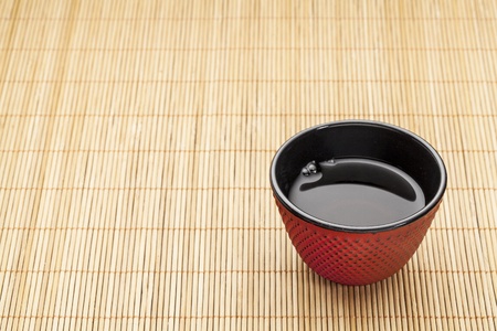 Japanese cup of tea on a bamboo mat - a traditional cast iron red hobnail design with black enamel insideの写真素材