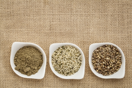 hemp products: seeds, hearts (shelled seeds) and protein powder in small ceramic bowls on burlap canvasの写真素材