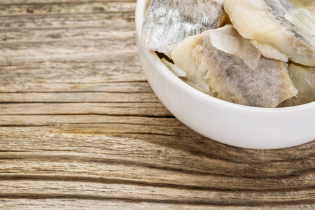 herring in wine sauce with  onion and spices - white sauce dish on grained woodの写真素材