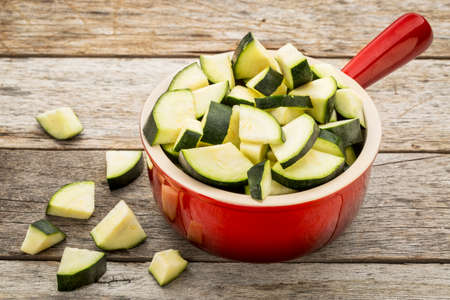 diced and sliced zucchini in red stoneware pot against rustic wooden tableの写真素材