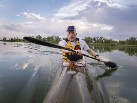senior male is  paddling racing sea kayak  on a calm lake with storm clouds in background, Fort Collins, Coloradoの写真素材